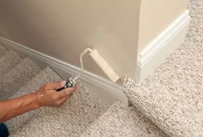 person's hand holding a paint roller, applying beige paint to a wall of Port St Lucie house