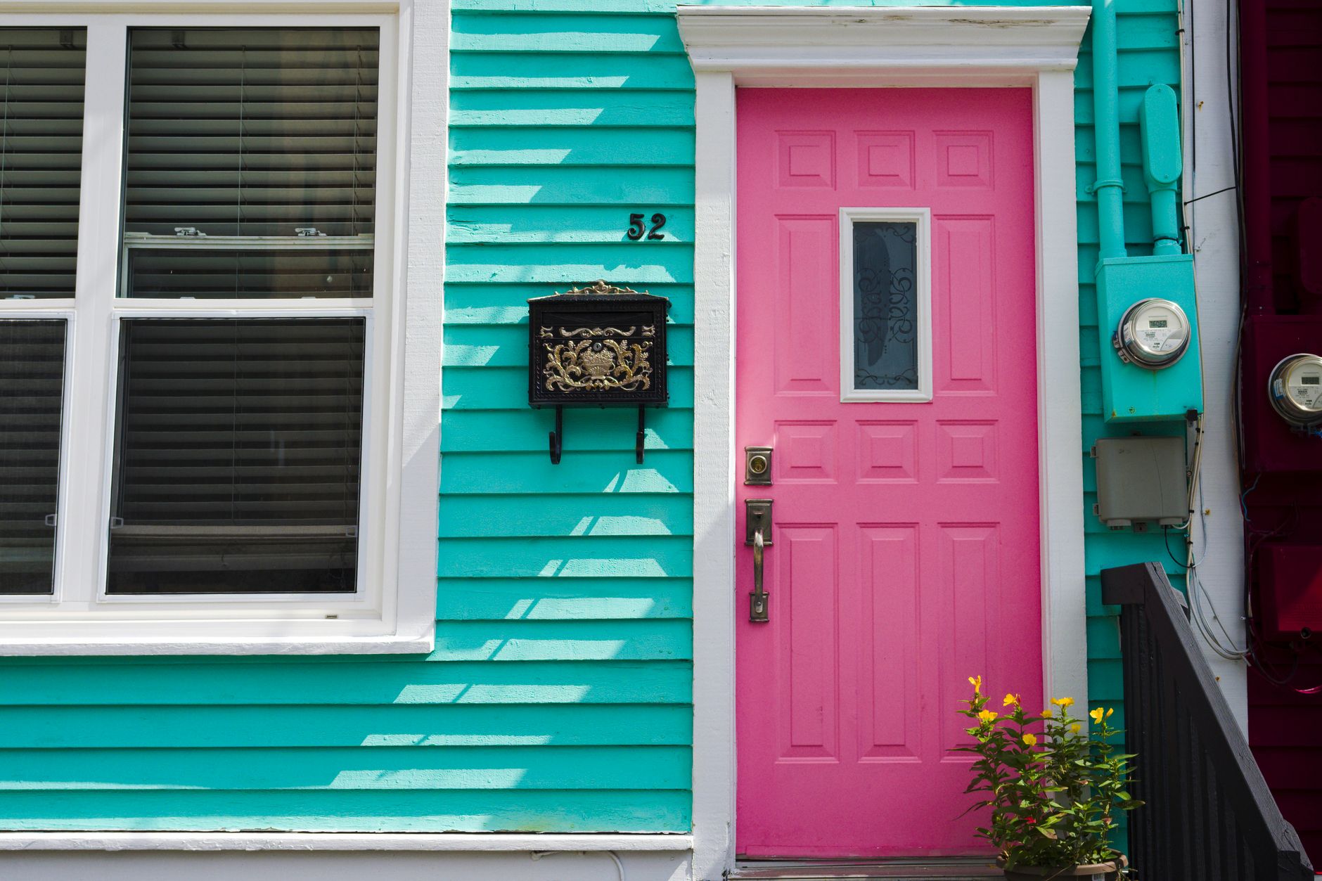 Colorful townhouse facade with a pink door and teal siding, showing how trim and accent colors affect house painting cost