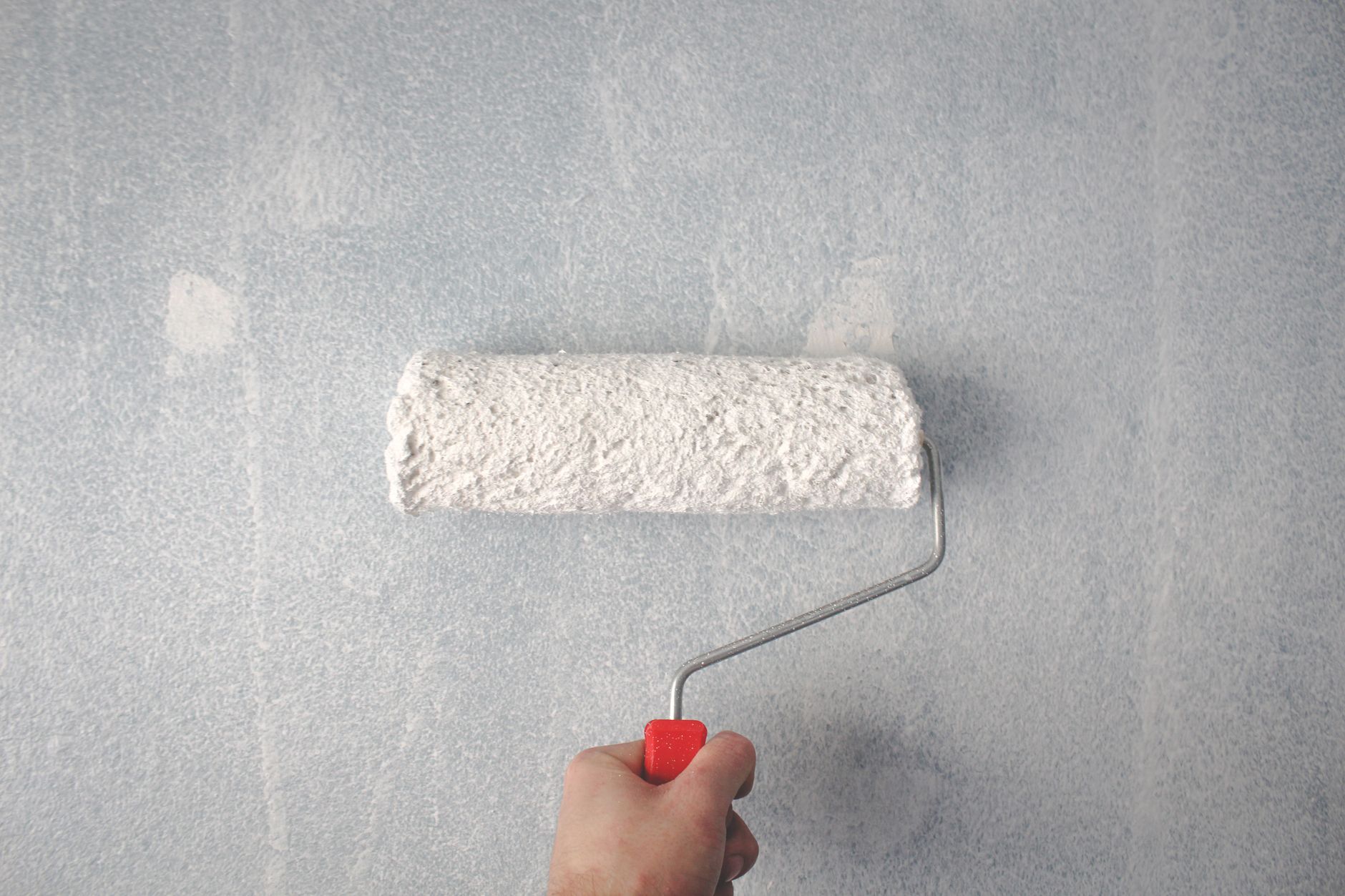 A person's hand using a paint roller to apply white paint on a wall